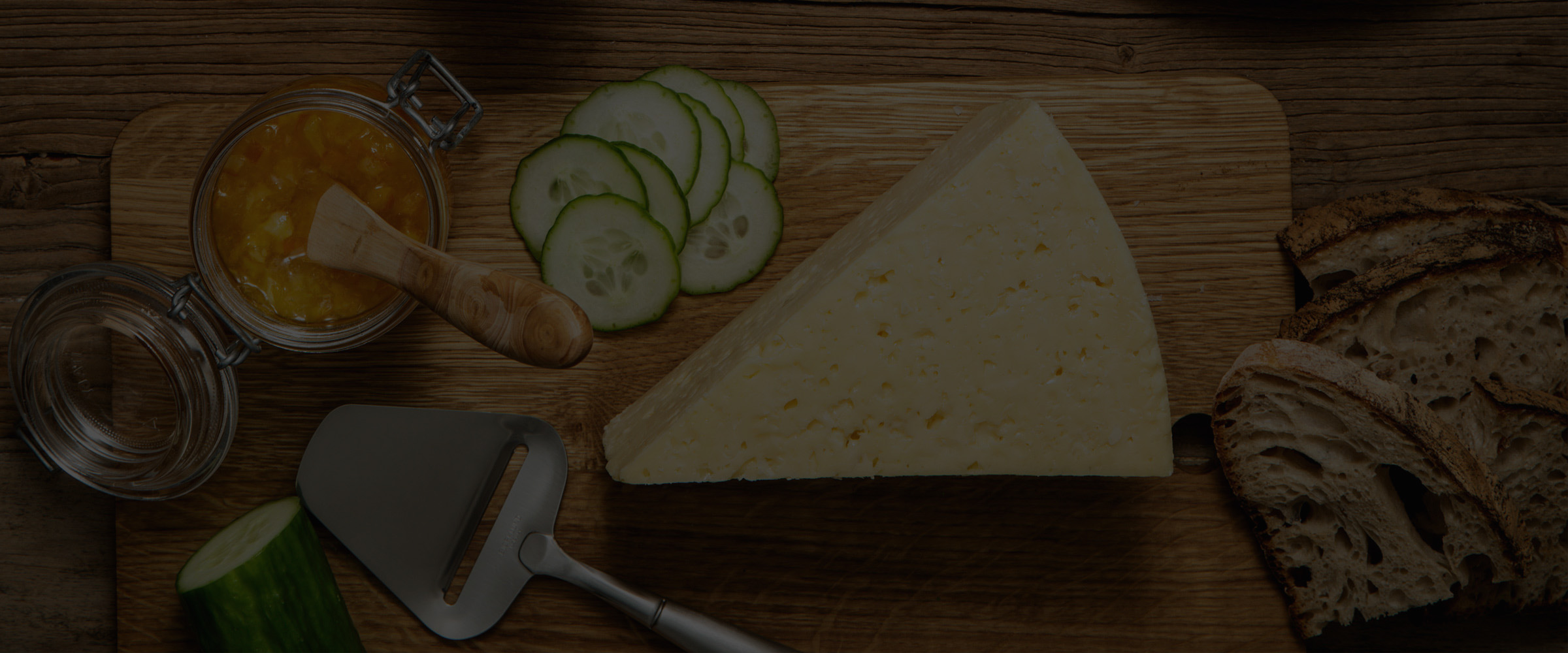 Prästost på en skärbräda med en osthyvel och gurkskivor